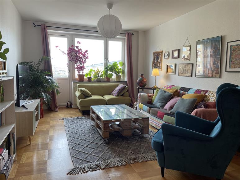 Vardagsrum med TV, en 2-sits och en 3-sitssoffa samt en fåtölj. Utgång till balkongen mot gatan.