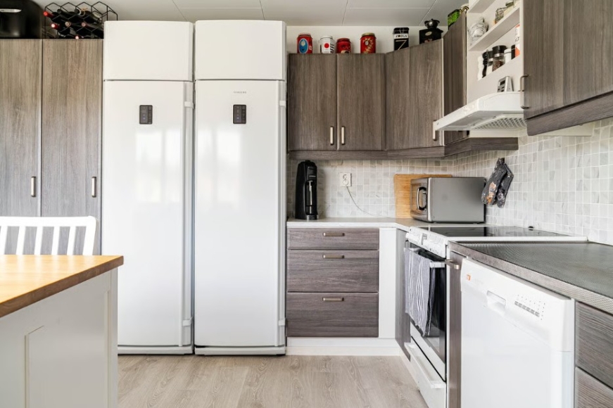 Kök med stor kyl och frys, spishäll, diskmaskin och microvågsugn. Köksö med barstolar.